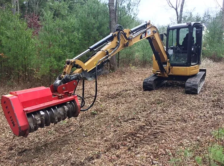 A small excavator is sitting in the middle of a forest.