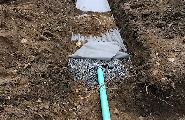 A green pipe is laying in the dirt next to a bag of gravel.