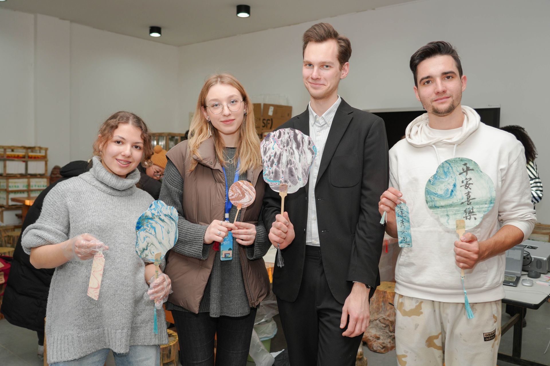 Four people holding up decorated paper fans indoors.