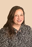Woman with long brown hair smiles, wearing a gray top with white dots against a light background.