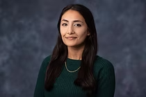 Woman with dark hair, wearing a green sweater and a gold chain, smiling at the camera.