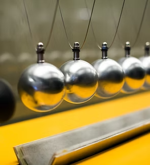 Newton's Cradle: Silver spheres hanging in a row, demonstrating momentum transfer. Yellow base.