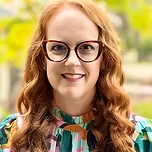 Woman with red hair and glasses smiles.