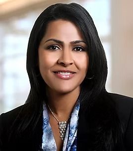 Woman with dark hair, smiling, wearing a black blazer and patterned scarf, necklace.
