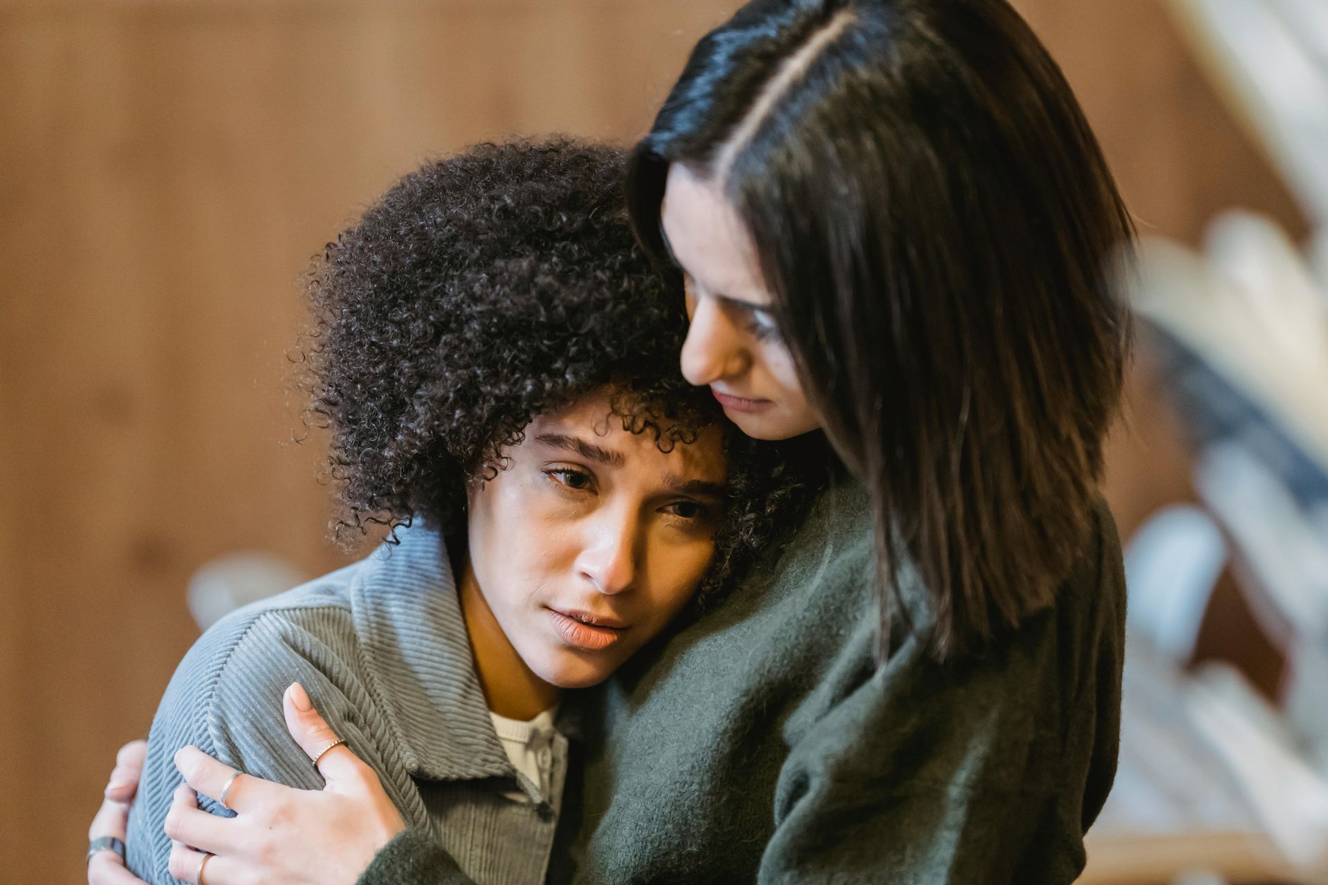 Two women hugging, one looking distressed, in an interior setting. One woman is offering comfort.