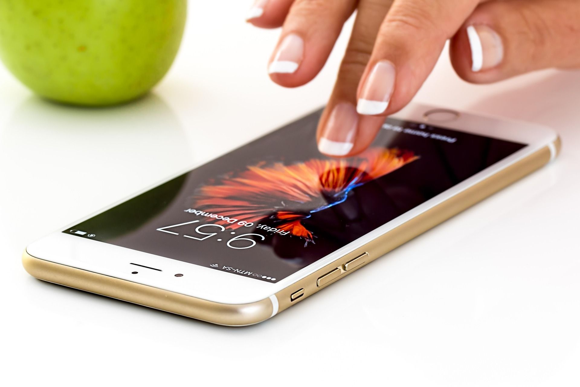 Hand tapping a gold smartphone displaying a colorful abstract design, green apple in the background.
