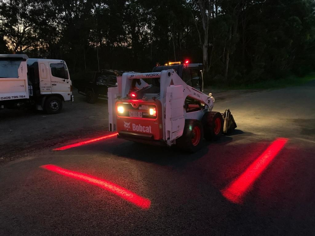 Bobcat Tractor is Driving Down a Road at Night — JP Civilworx Pty Ltd in Port Macquarie, NSW