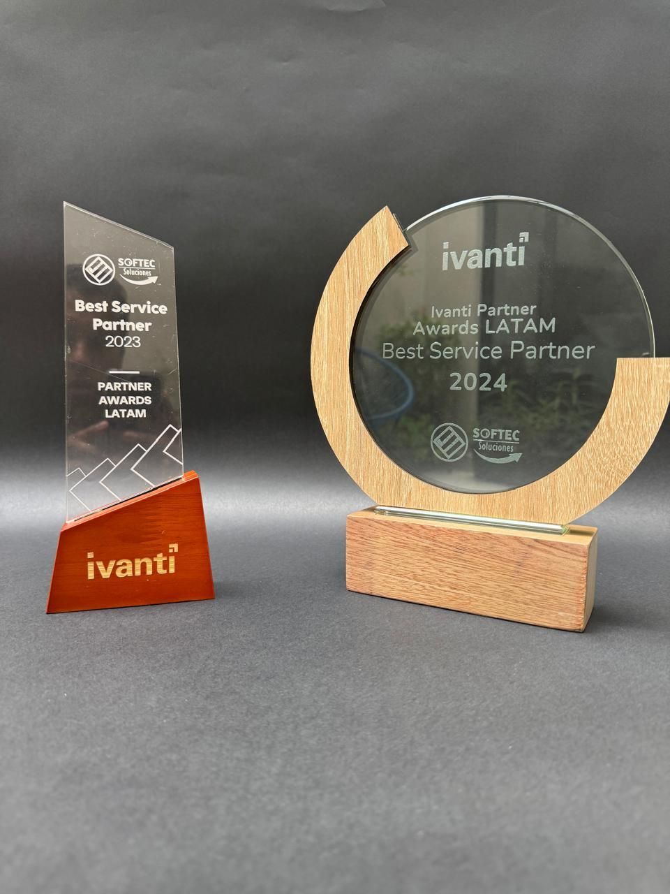 Dos premios: uno rectangular y otro circular. Ambos tienen base de vidrio transparente y madera. El logo de Ivanti evisible.