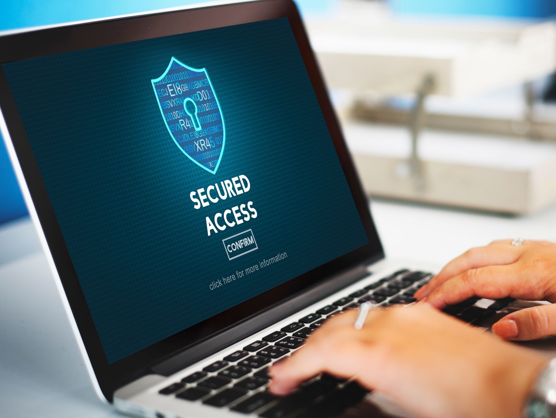 A person is typing on a laptop computer with a shield on the screen.