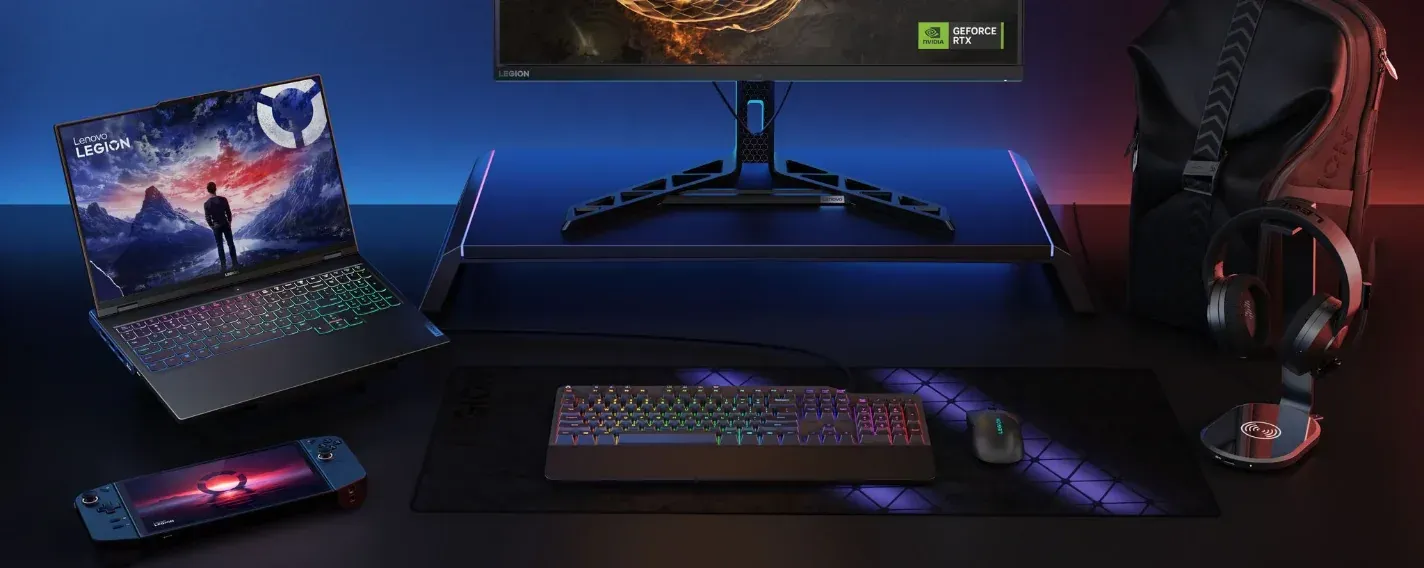 Configuración de juego con una computadora, monitor, teclado, consola de juegos y auriculares iluminados con luz azul y roja.