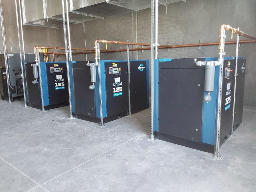 A row of air compressors are lined up in a room.