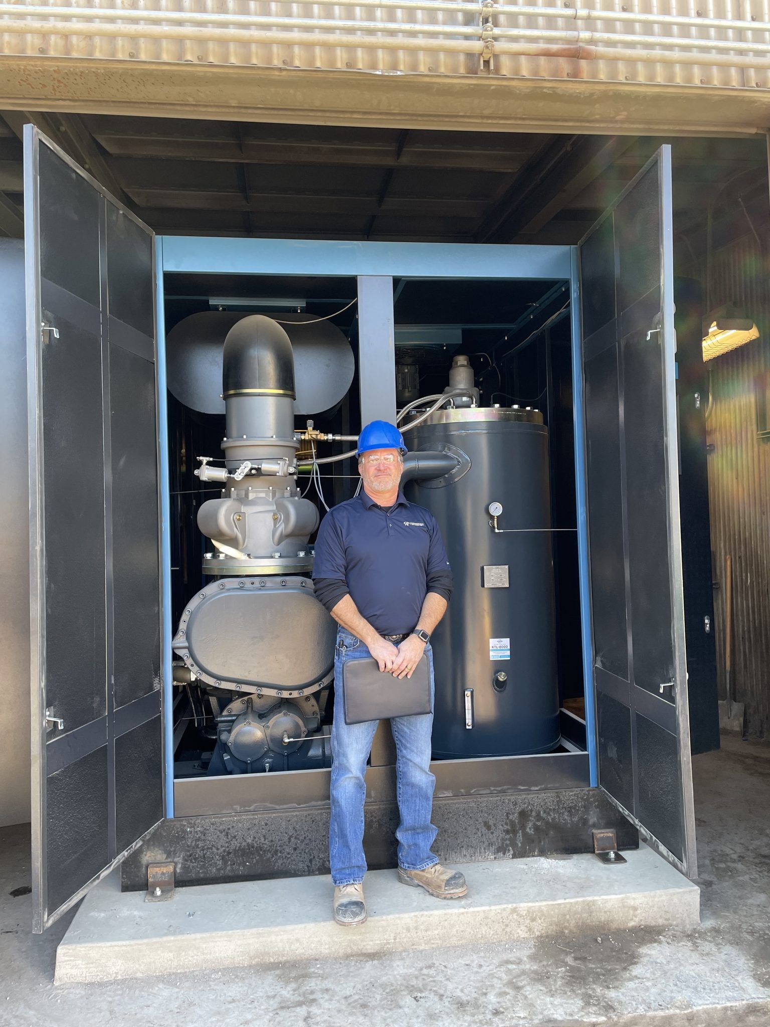 A man in a blue hard hat is standing in front of a machine.