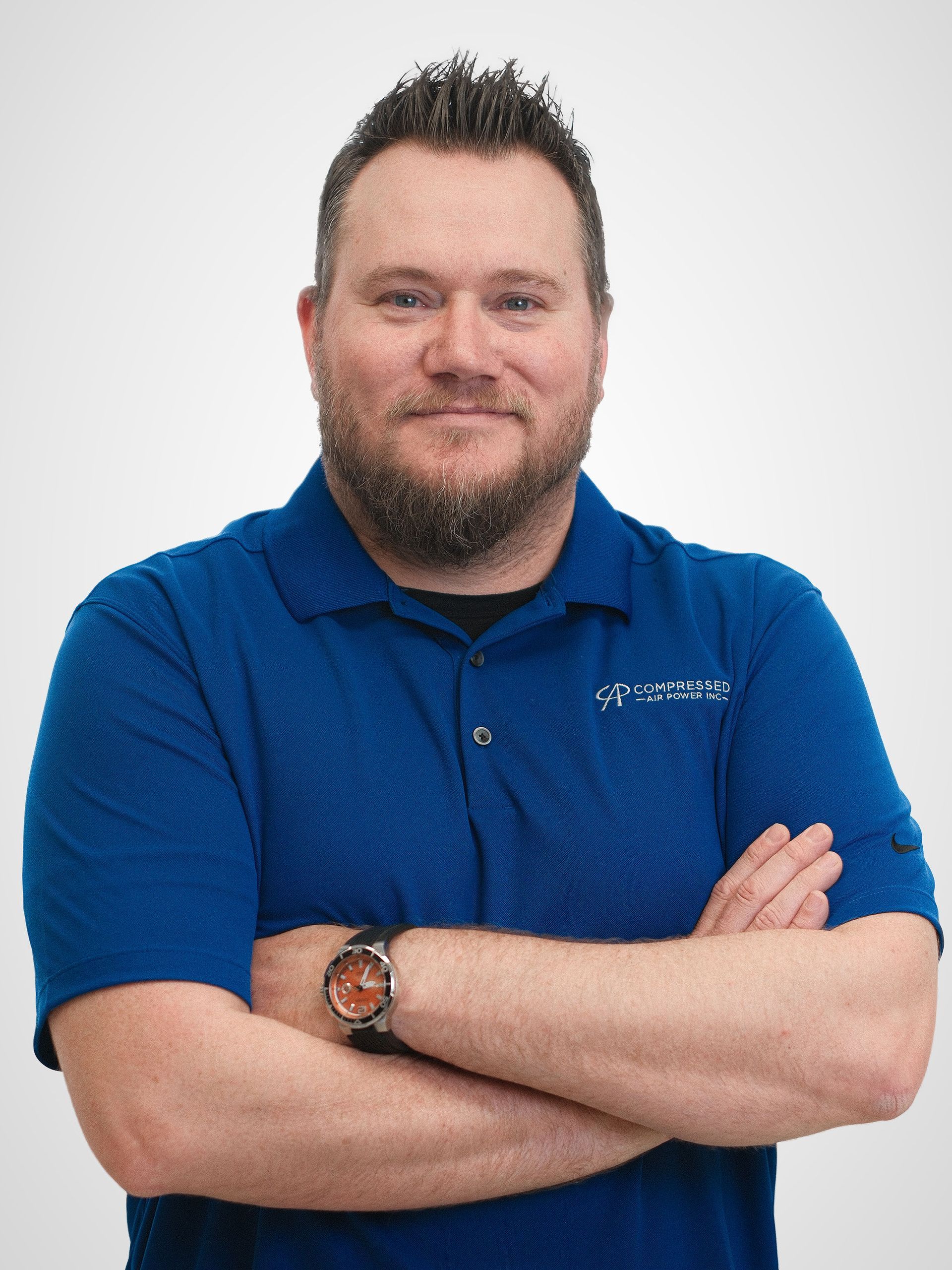 A man in a blue shirt is standing in front of a white background.