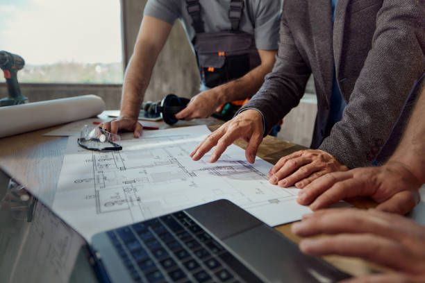 A group of men are looking at a blueprint next to a laptop.