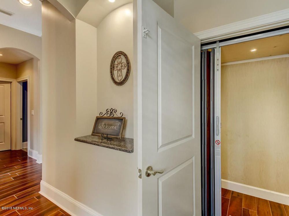 Hallway with wood floor, white door, small shelf with decoration, and open closet.