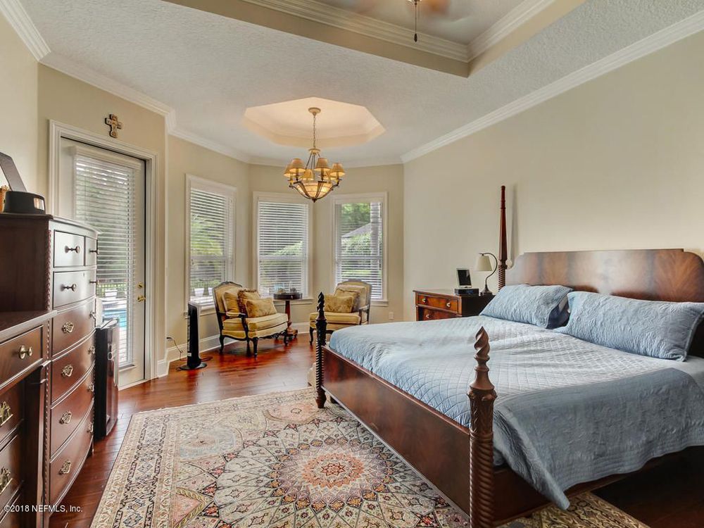 Bedroom with dark wood furniture, ornate rug, and seating area by windows.