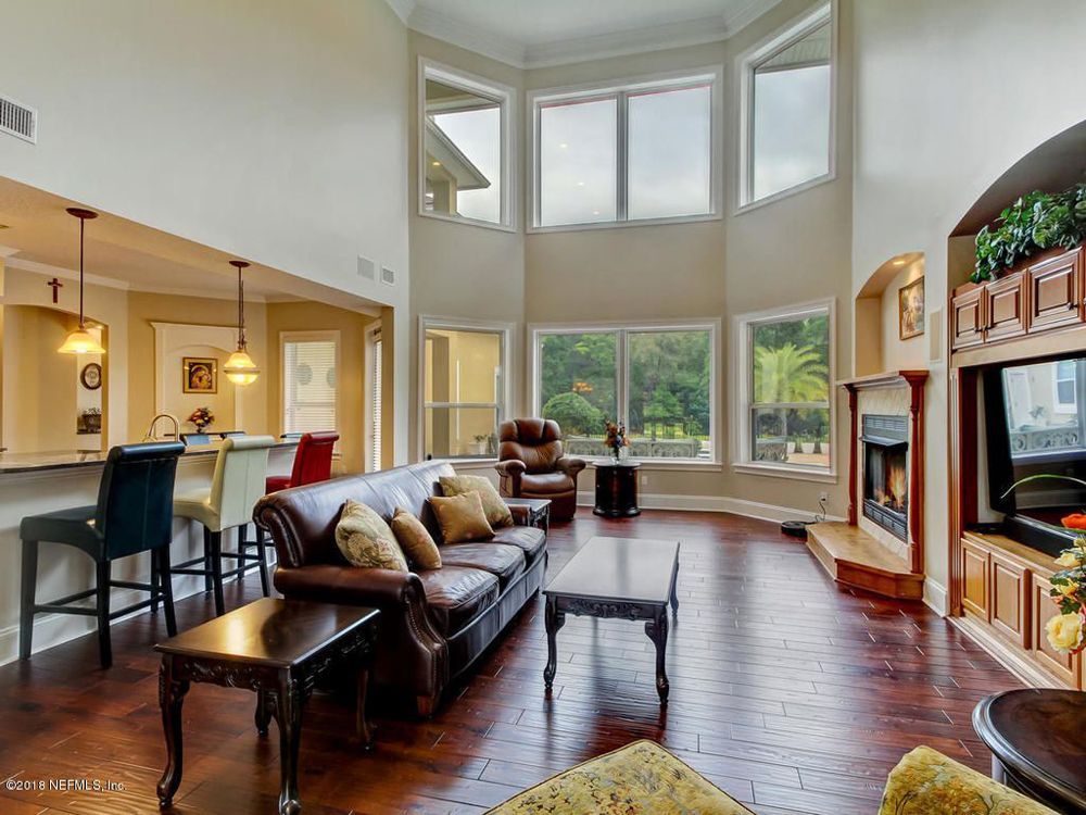 Spacious living room with a leather sofa, fireplace, and large windows overlooking a green space.