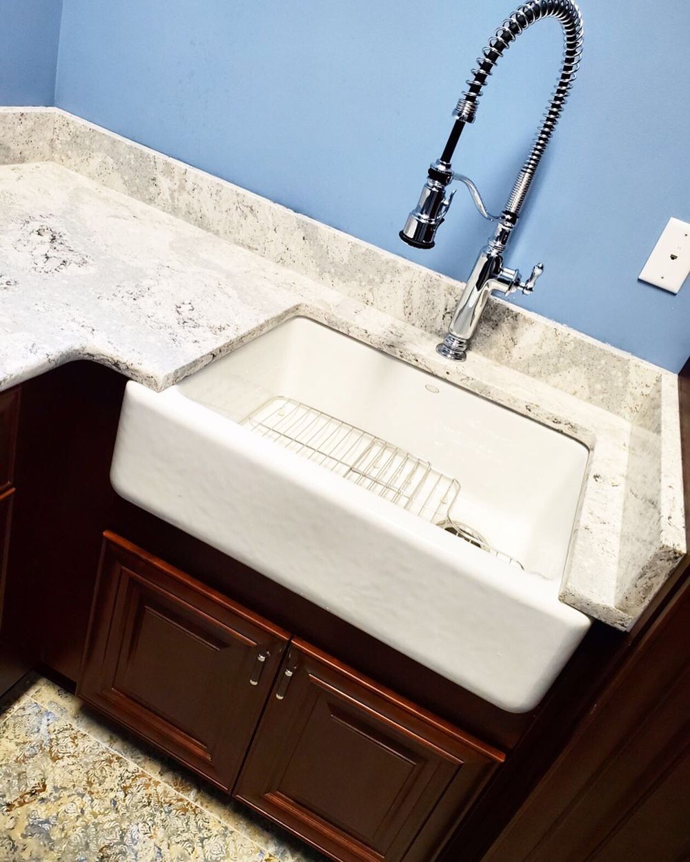 White farmhouse sink with pull-down faucet, granite countertop, dark cabinets, and blue wall.