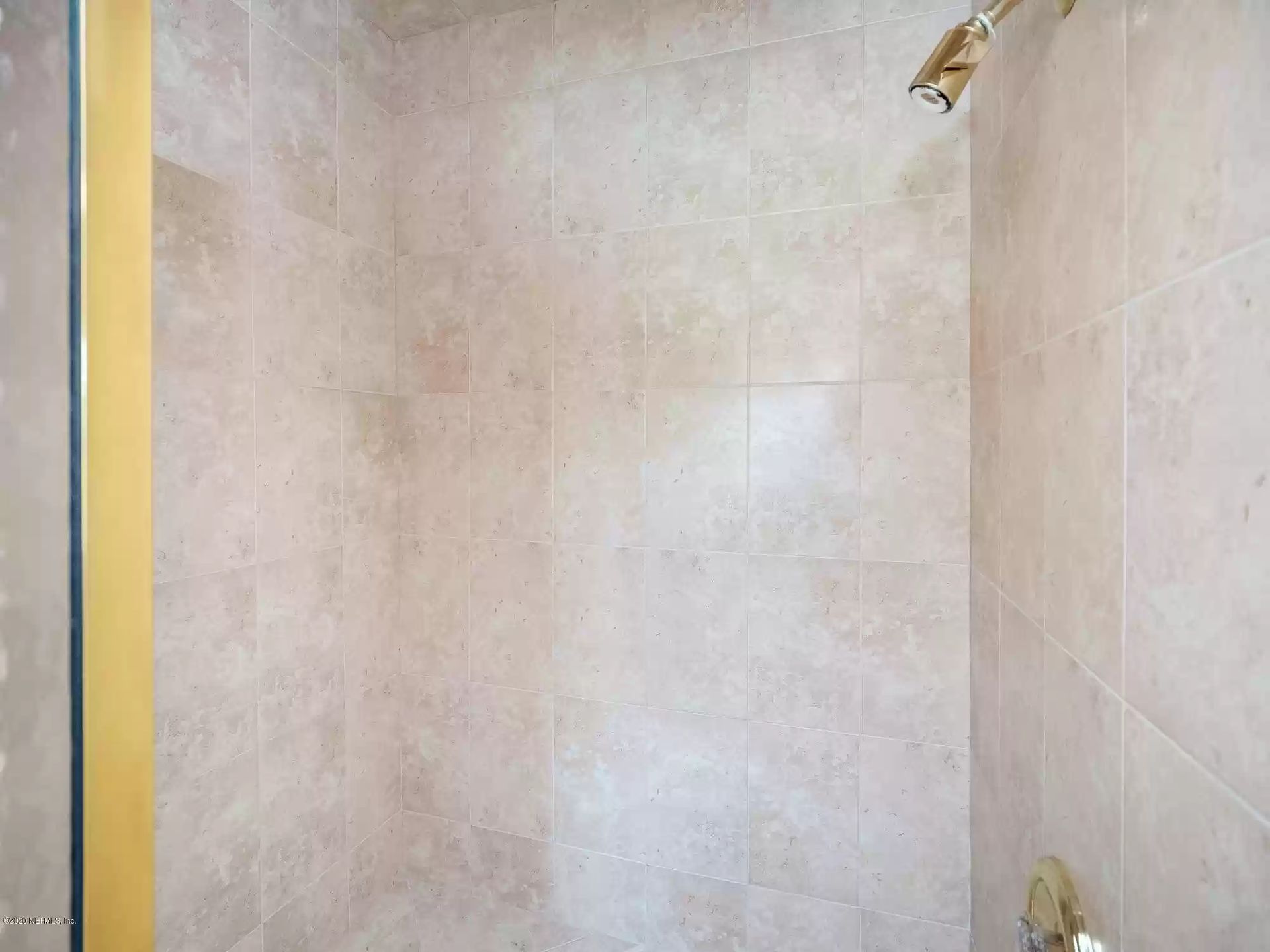 Beige tiled shower with gold showerhead.