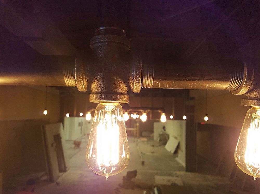 Industrial pipe light fixture with Edison bulbs in a construction setting.