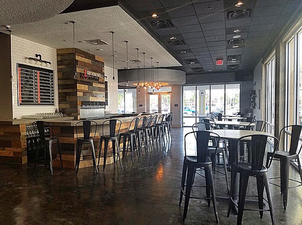 Restaurant interior: Bar with wood paneling, metal chairs, tables, large windows, and dark flooring.