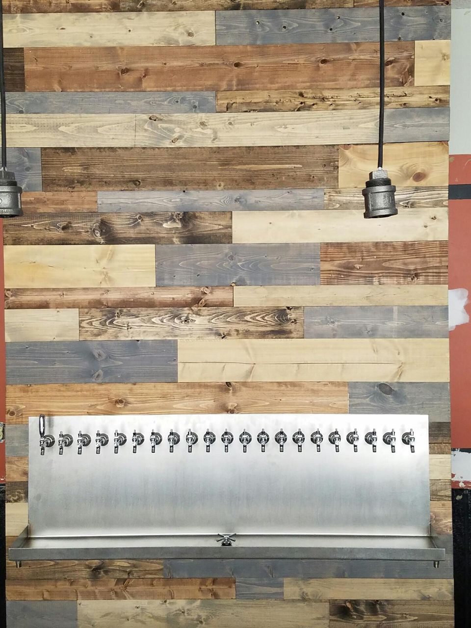 A bar with multiple beer taps against a wooden plank wall; two pendant lights hang above.