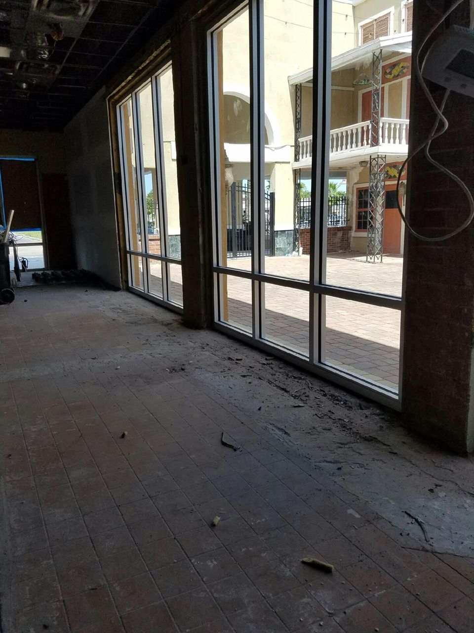 Empty room with large windows, showing exterior courtyard. Dirty wooden floor, exposed ceiling beams.