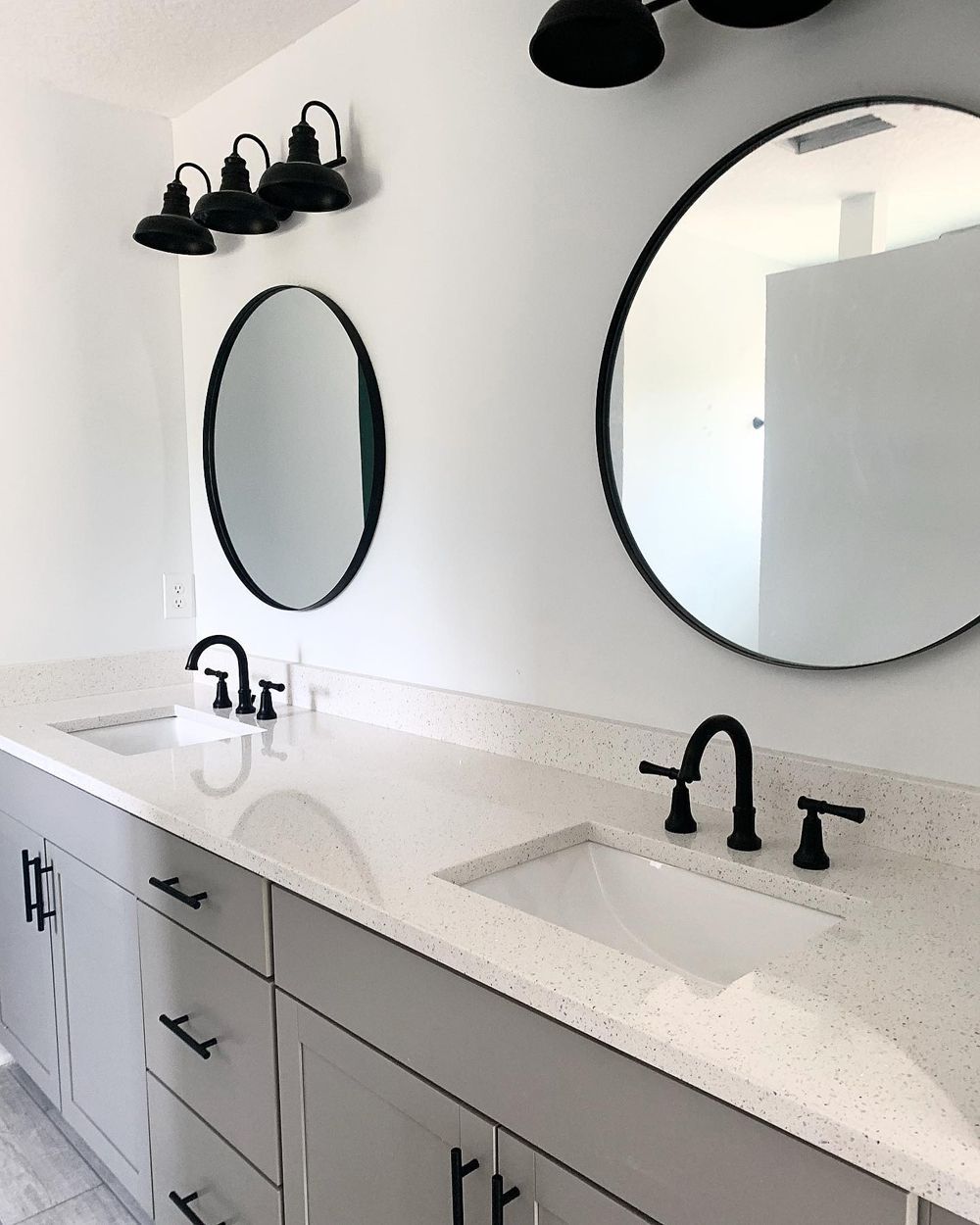 Bathroom with gray cabinets, white countertops, black fixtures, and round mirrors.