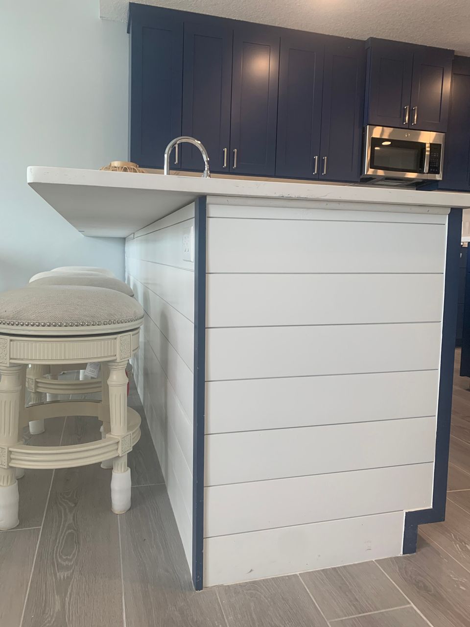 Kitchen island with white shiplap siding, blue trim, and blue cabinets. A stool sits at the counter.