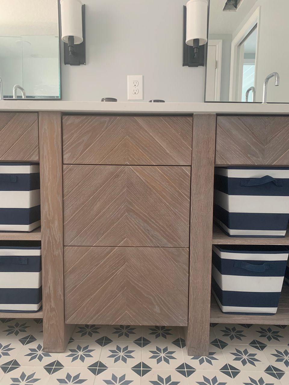 Bathroom vanity with a light-wood, chevron patterned center and shelves holding blue and white striped bins.