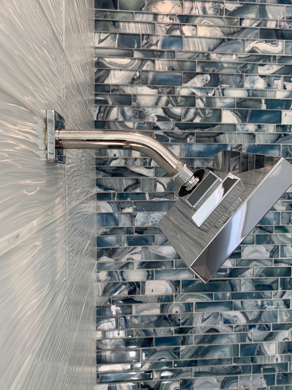 Chrome showerhead against a blue and white mosaic tile wall.
