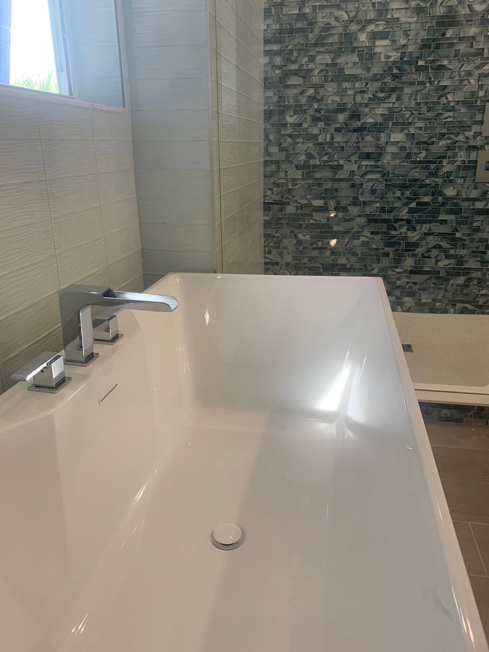 White bathtub with chrome faucet in a modern bathroom, next to a textured, patterned wall.