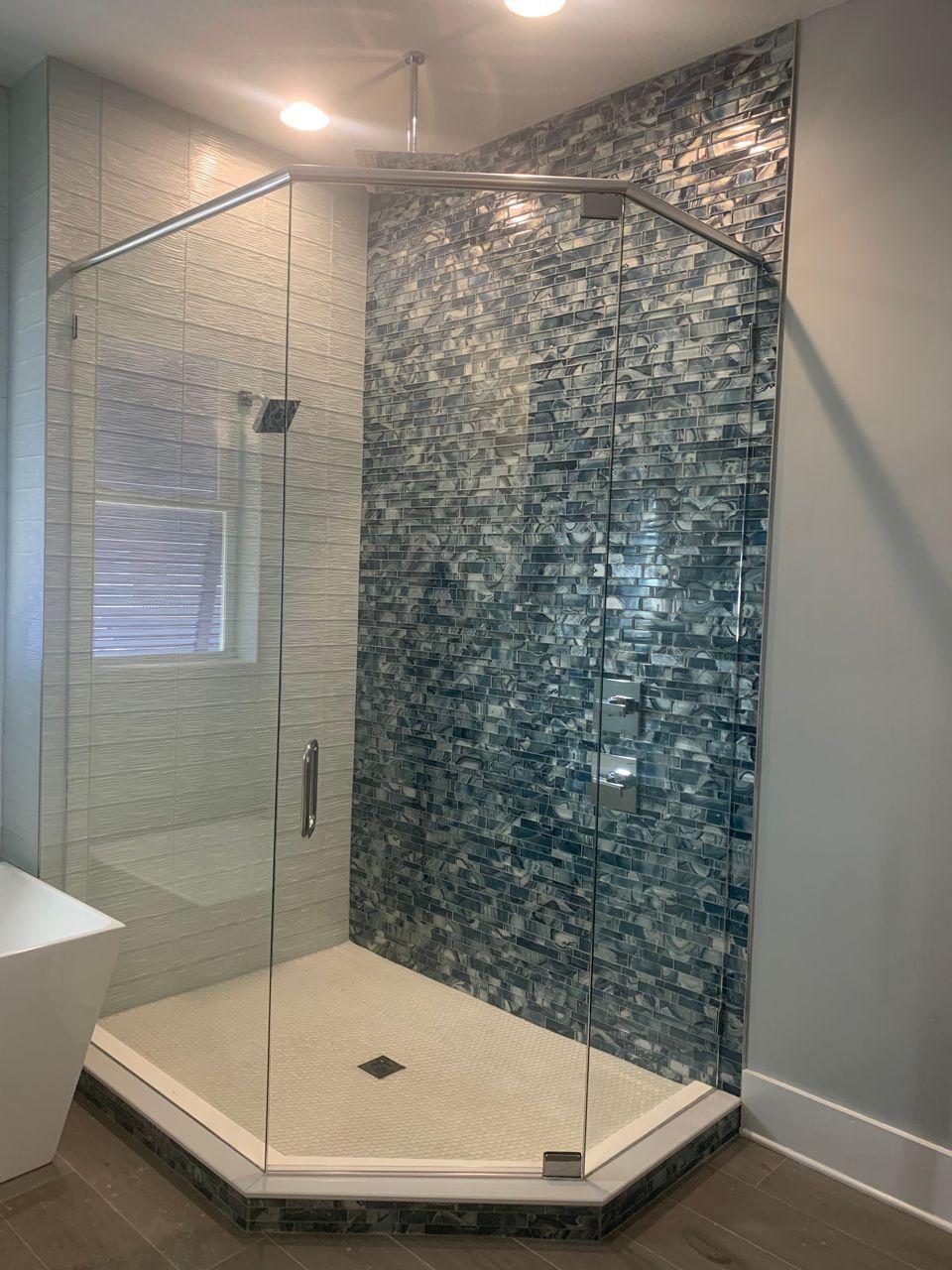 Modern bathroom with glass shower, teal accent tile, and light-colored walls and floor.