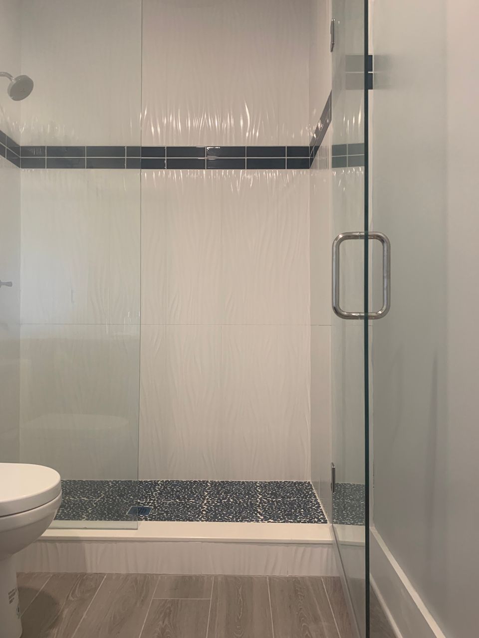 Shower stall with white tile walls, blue tile floor, glass door and gray wood-look tile floor.