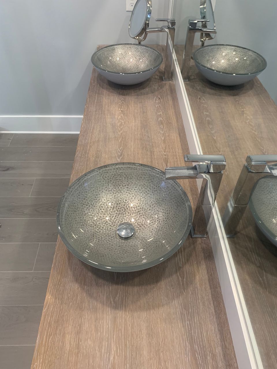 Three bowl sinks with chrome faucets sit on a wood counter, near a mirror, in a bathroom.