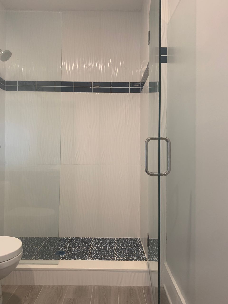 A modern white tiled shower with glass doors, dark pebble floor, and dark blue accent tiles.