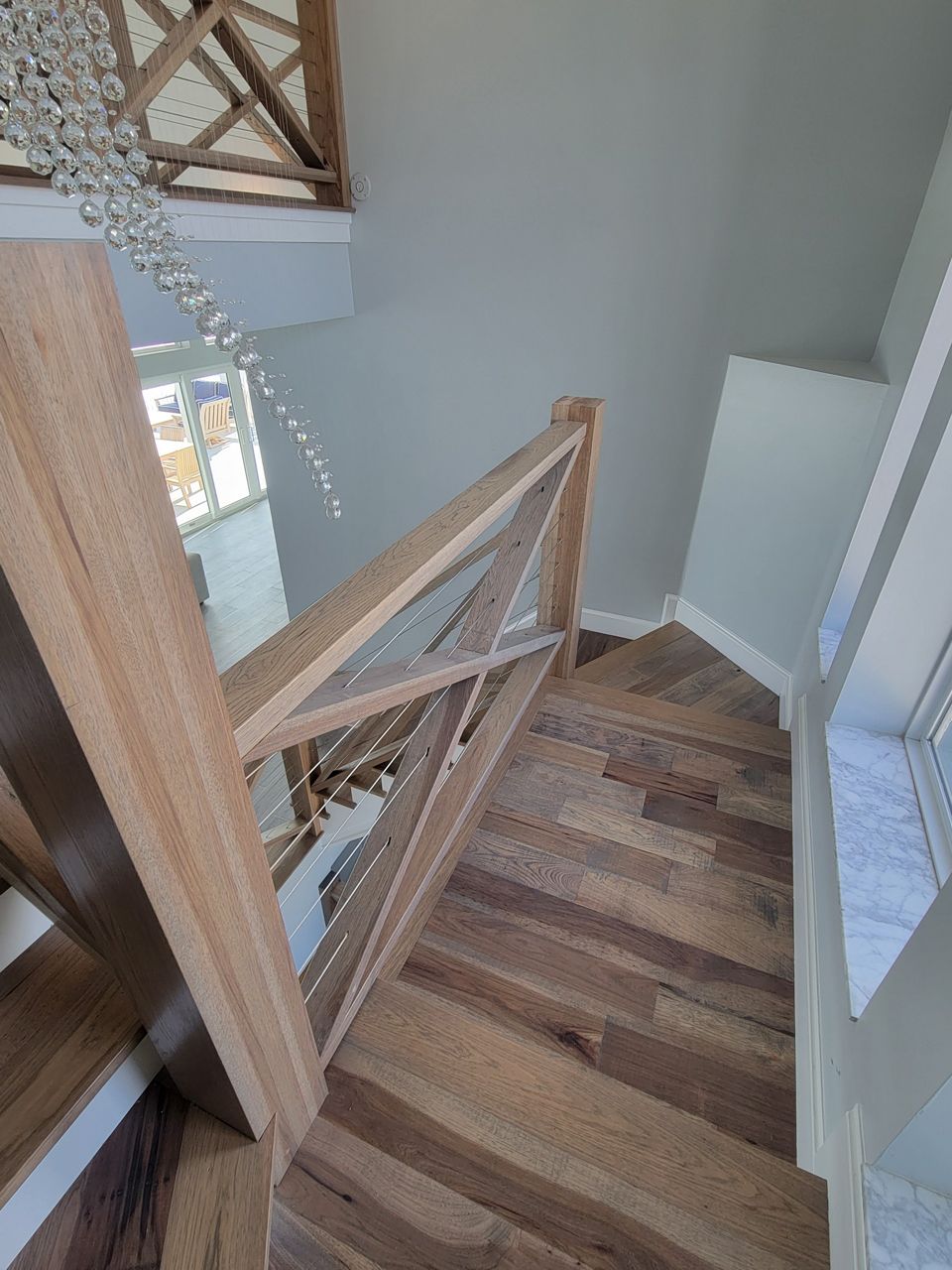 Wooden staircase with light wood railings, leading down from an upper level with natural light.