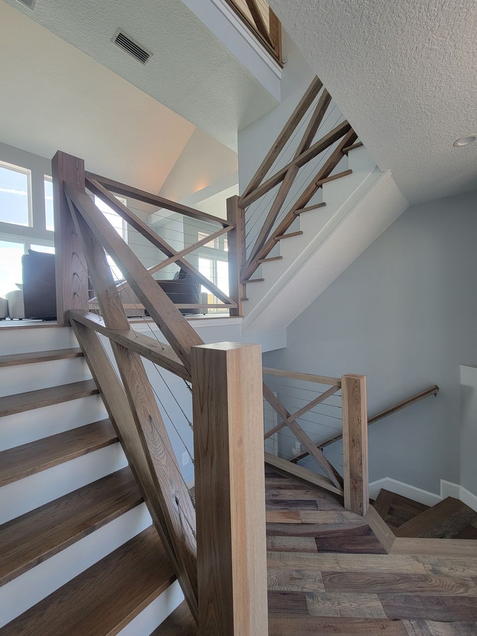 Wooden staircase with rustic handrails and cable railing in a brightly lit home.