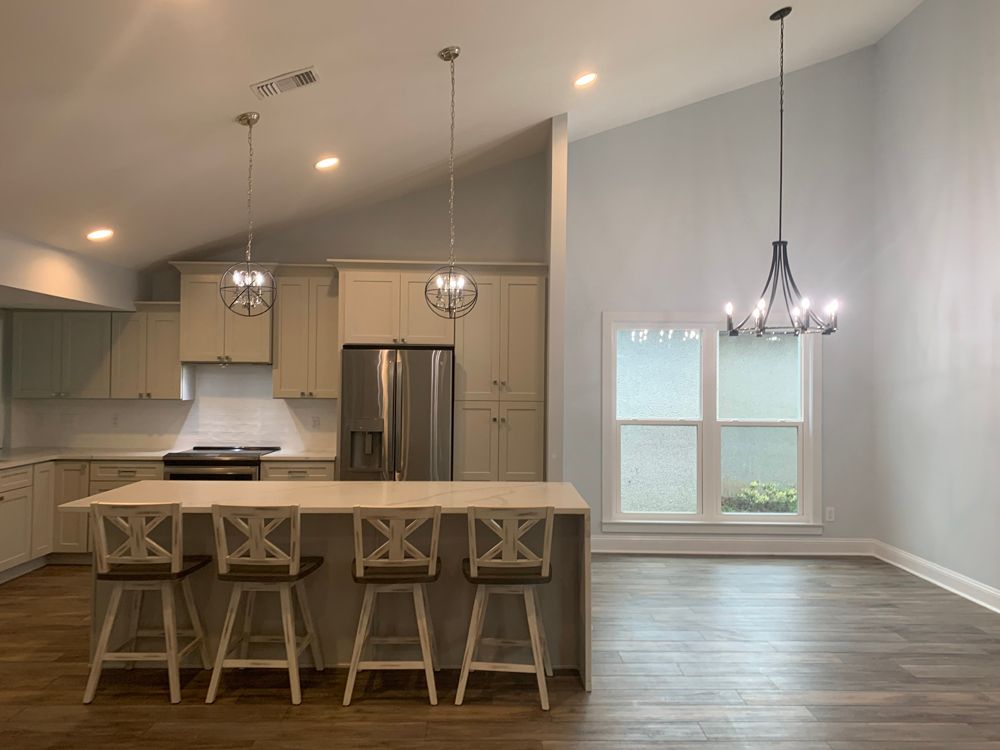 Modern kitchen with island seating, stainless steel appliances, and light-colored cabinets; light blue walls, wood flooring.