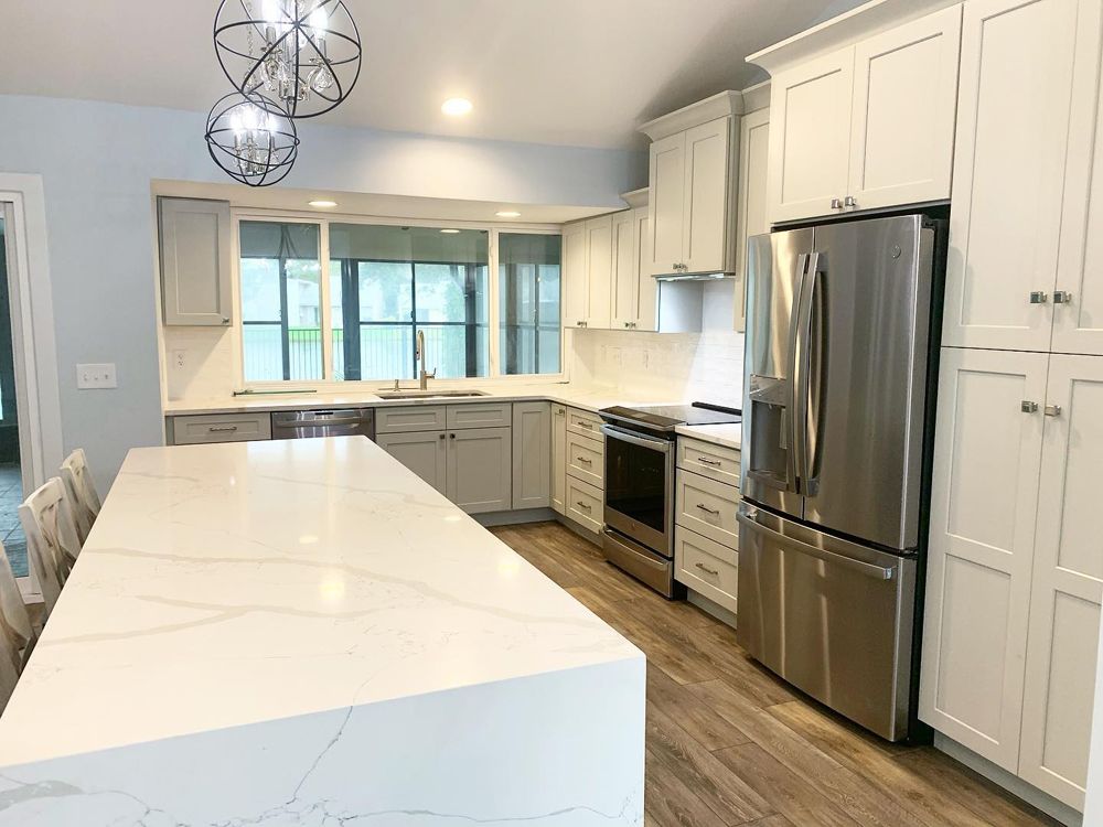 Spacious modern kitchen with white cabinets, island, stainless steel appliances, and light wood floors.