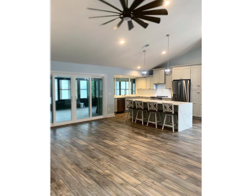 Spacious kitchen with wood floors, white cabinets, large island with bar stools, and sliding glass doors.