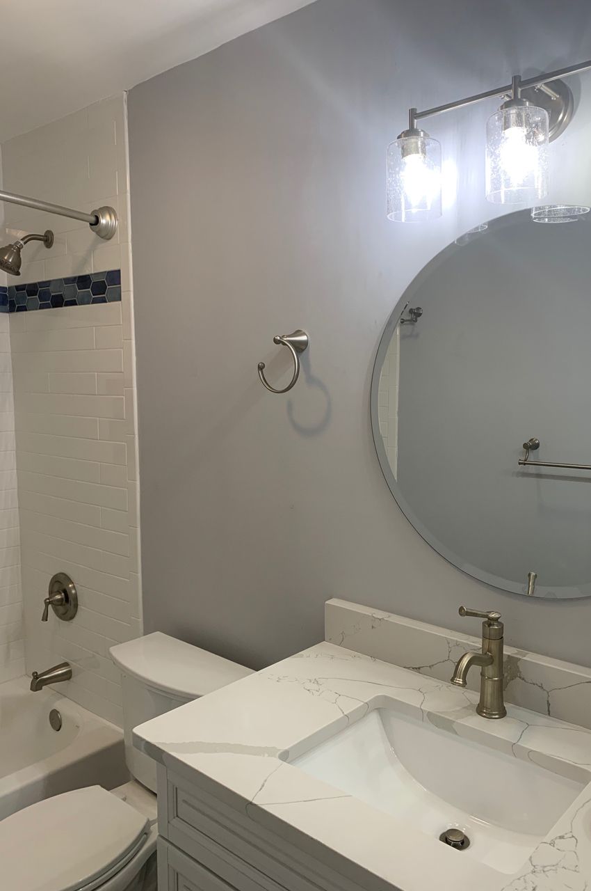 Bathroom with a gray wall, white vanity, round mirror, and silver fixtures.
