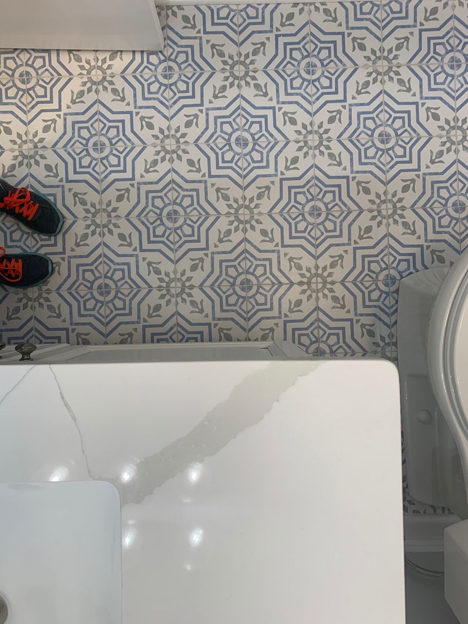 Blue and white patterned floor tile, white vanity and toilet, person's feet wearing black and orange sneakers.