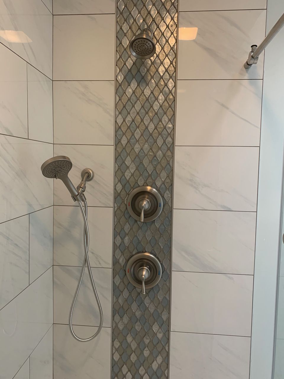 Shower with white tile and a decorative mosaic strip containing shower controls and head.