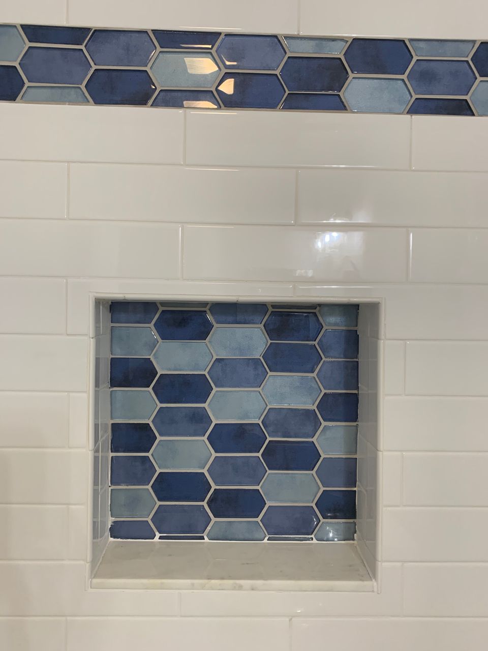 White tiled shower with blue and light blue hexagon-shaped accent tiles and a matching built-in niche.