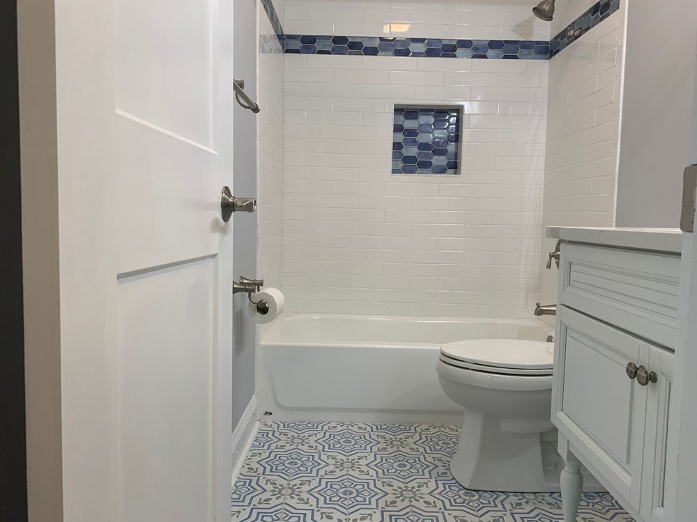 Bathroom with white tile shower, blue accent tiles, white toilet, and patterned blue tile floor.