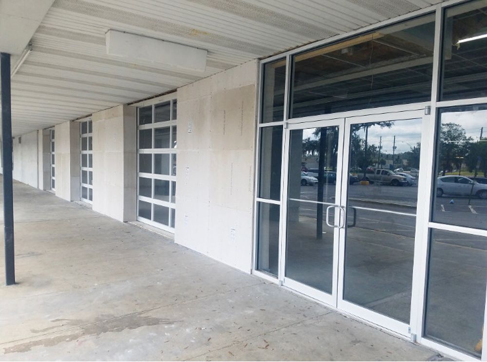 Exterior of a building with a covered walkway, glass doors, and windows, under a white awning, gray concrete flooring.