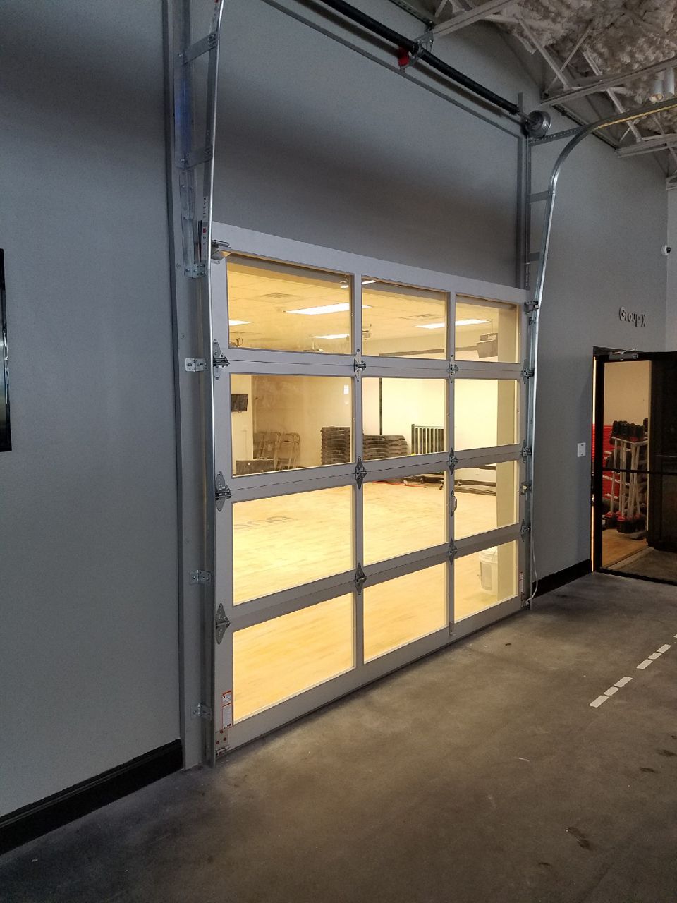 Glass garage door, open, revealing interior room with wood floor, and a doorway to another space.