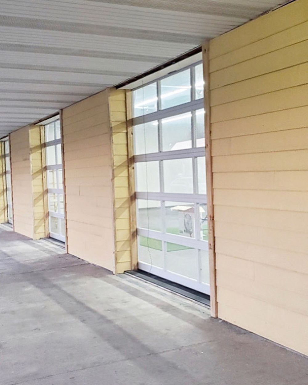 Light yellow siding surrounds glass doors in a hallway with a concrete floor.