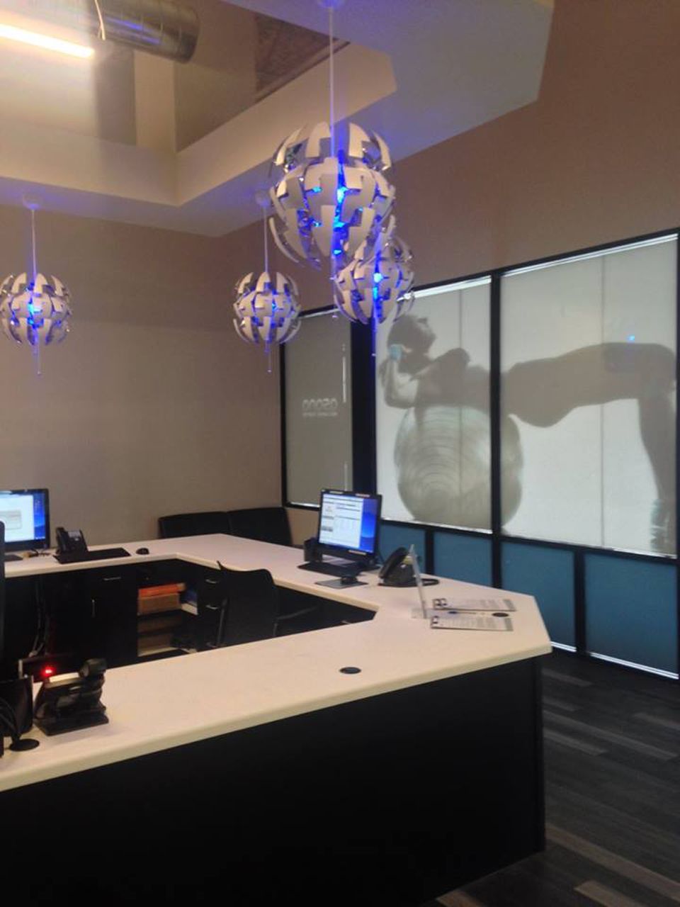Reception area with a black and white counter, pendant lights, and large window silhouettes of people exercising.